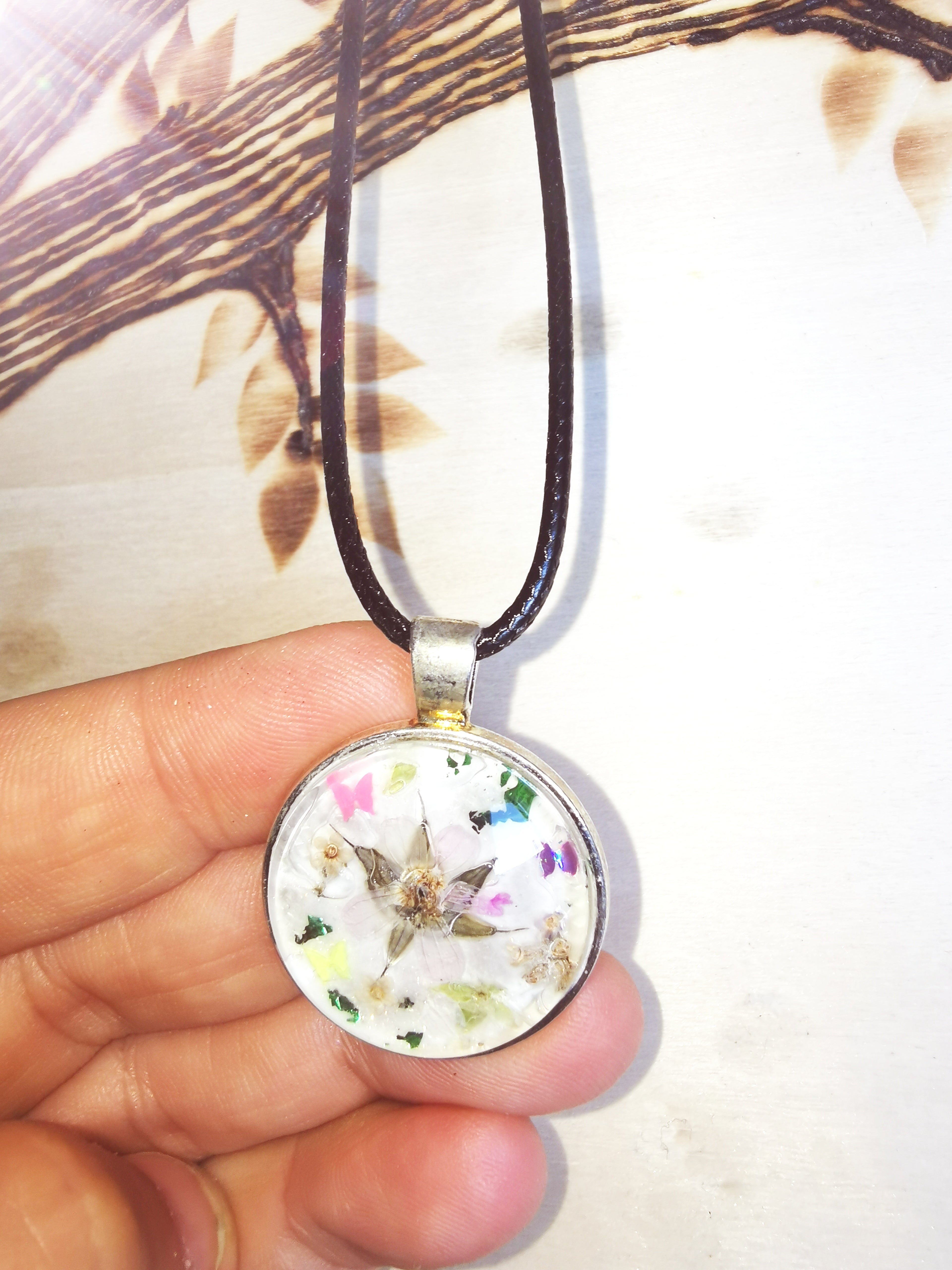 Pendentif fleuri en résine avec fleurs séchées et éclats colorés, porté sur un cordon noir.