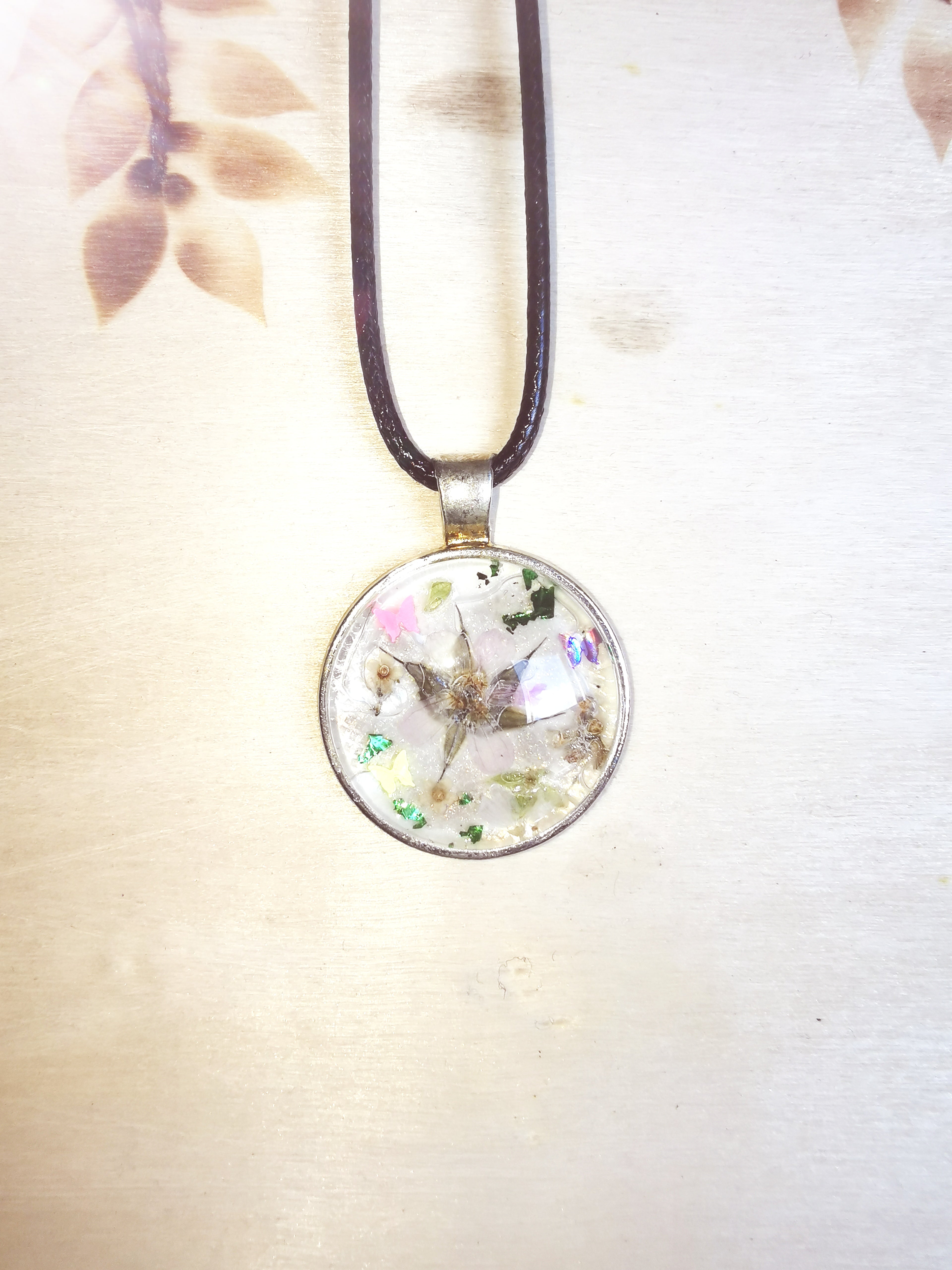 Pendentif fleuri en résine avec fleur séchée et décor coloré, cordon noir réglable inclus.