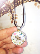 Pendentif fleuri en résine avec fleurs séchées et éclats colorés, porté sur un cordon noir.