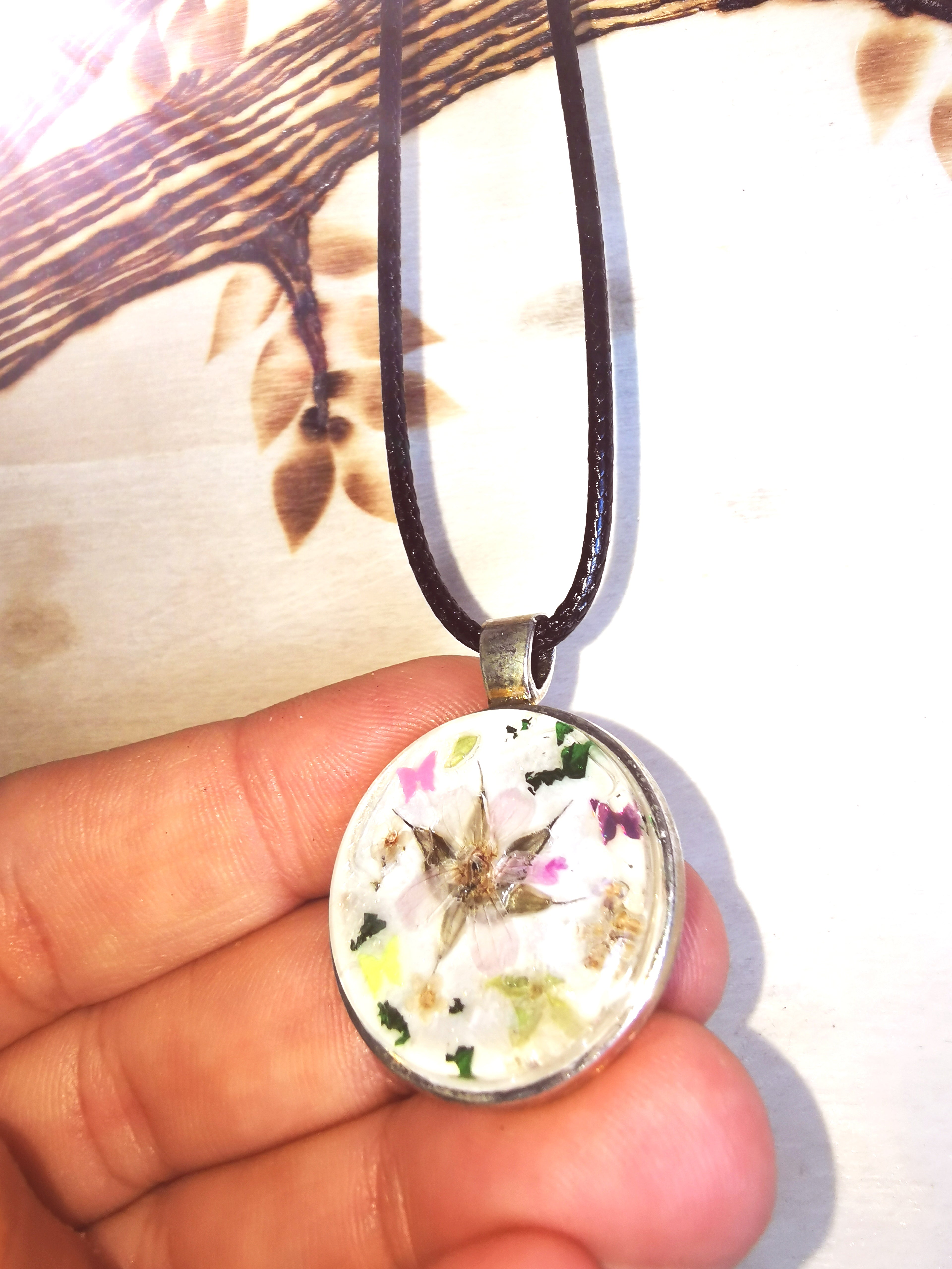 Pendentif fleuri en résine avec véritable fleur séchée et décor coloré, sur un cordon noir réglable.